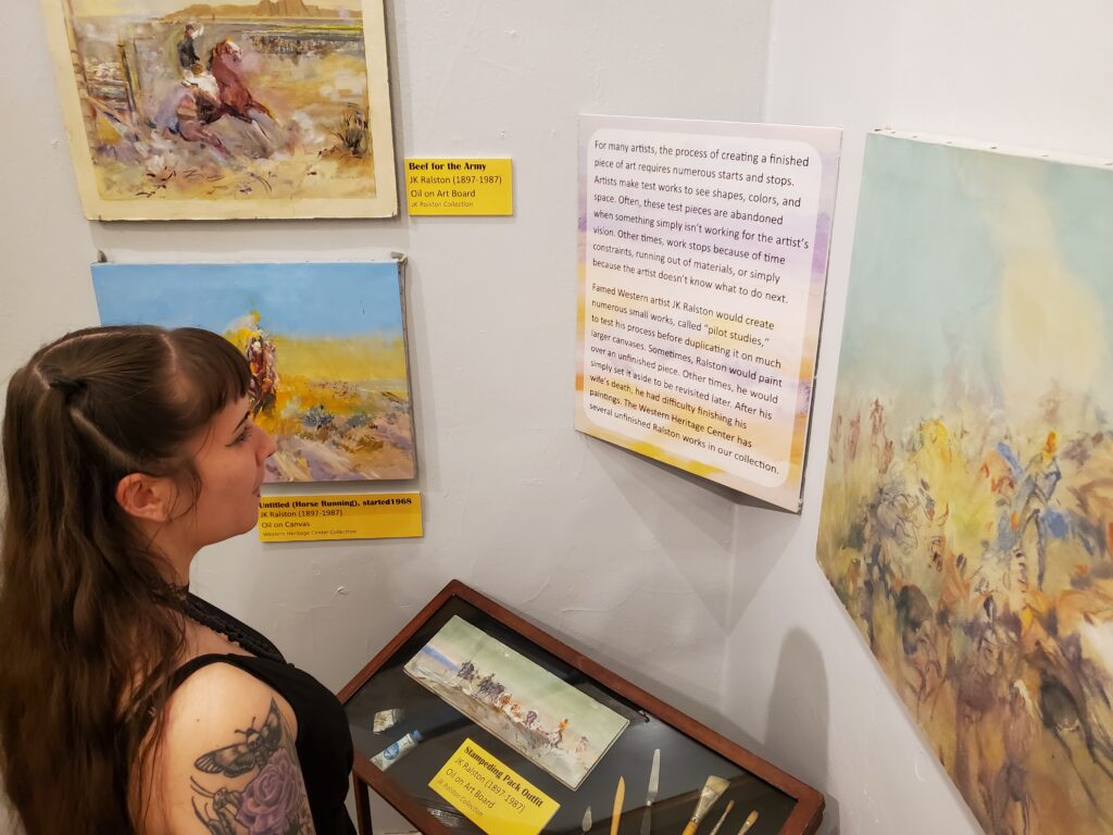 Woman in black sleeveless top reads museum panel surrounded by paintings