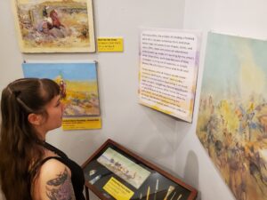 Woman in black sleeveless top reads museum panel surrounded by paintings