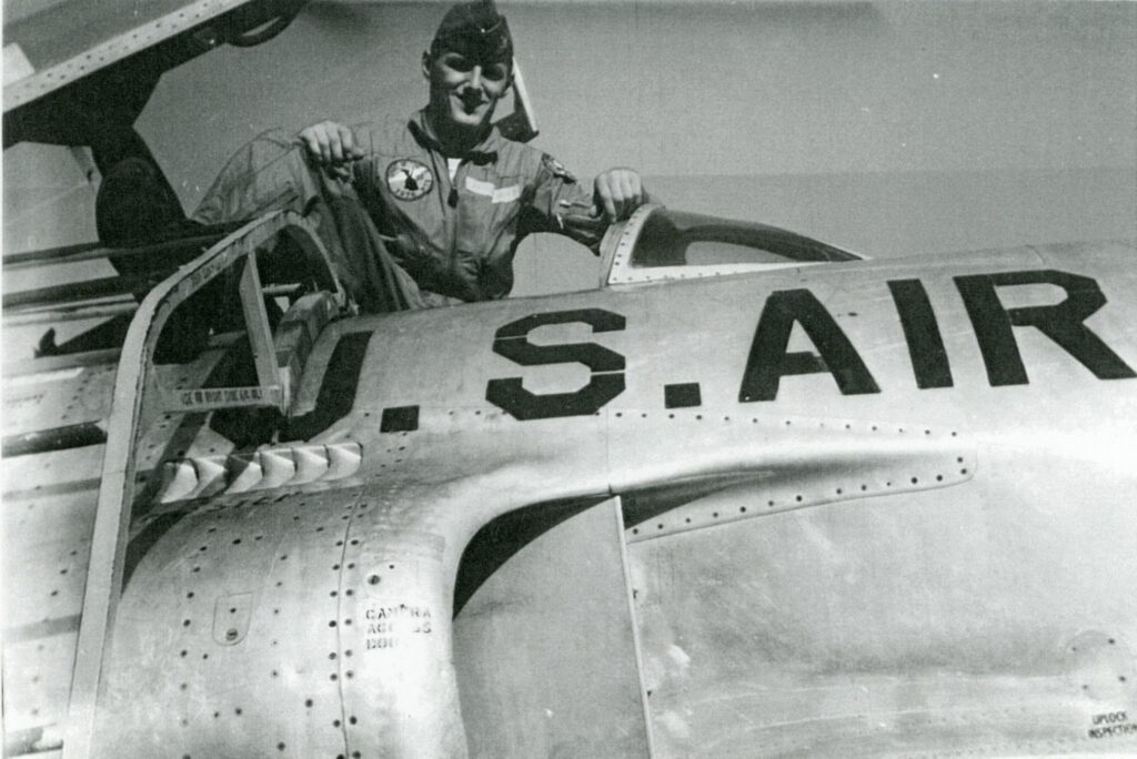 Man in military uniform sitting in the pilots seat of a T33a airplane with U.S. Air written on the side.